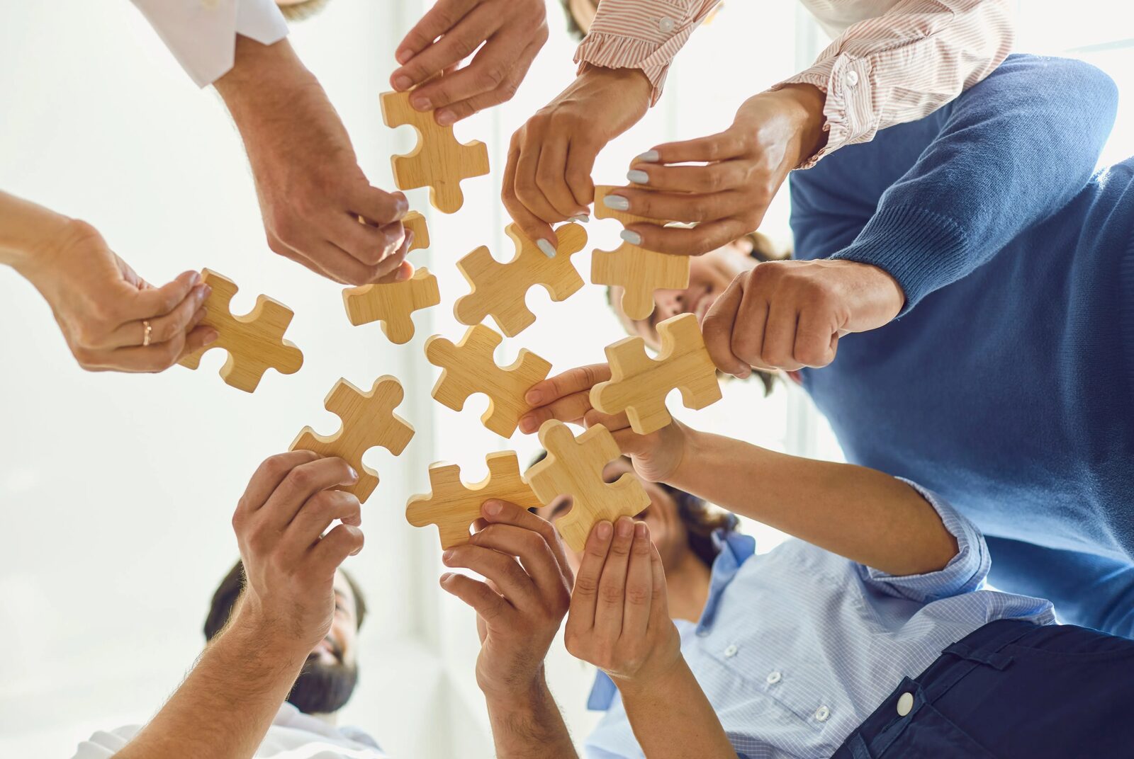 Several hands fitting jigsaw pieces together on a table