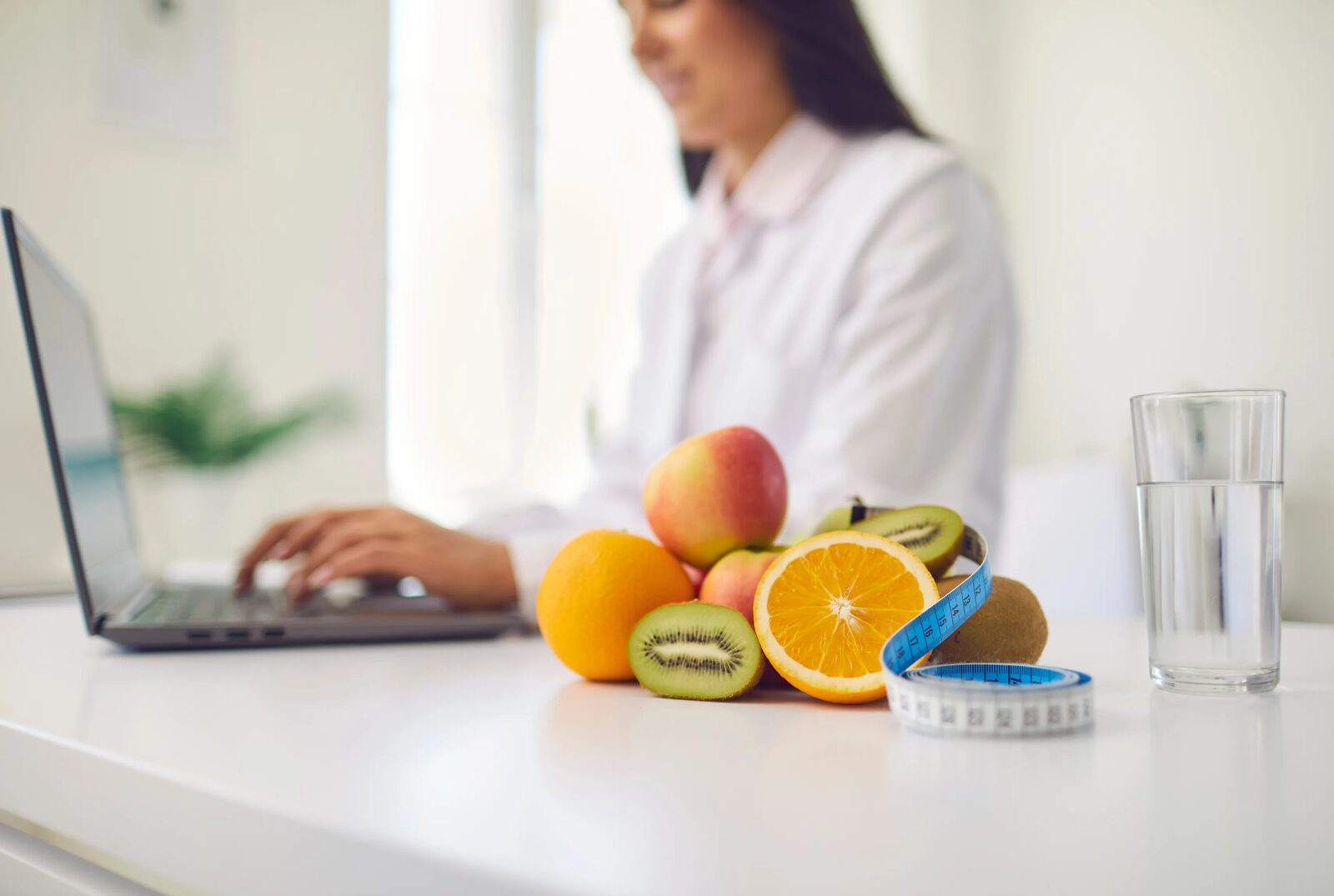 A person working at a laptop with fruit and a glass of water beside them on the desk